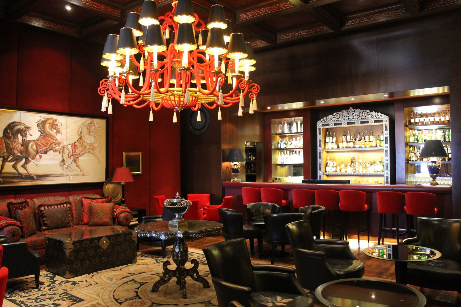 Salle d’un bar sous un grand lustre rouge, banquettes et comptoir